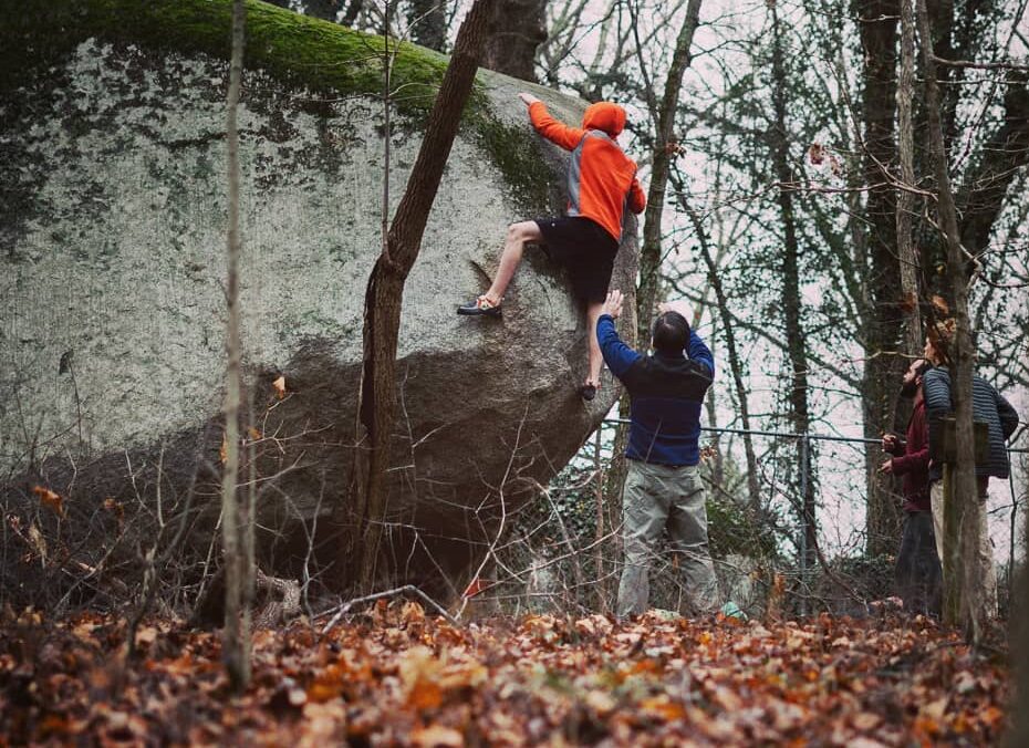 Rock climber bouldering on a boulder with a person spotting him. 